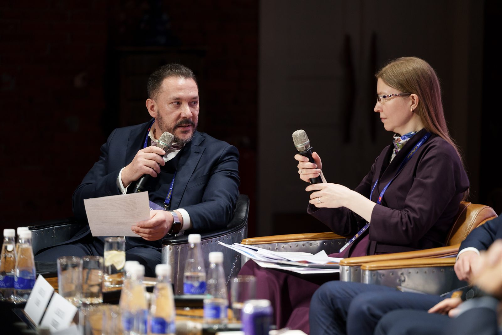 Sergei Solovev and Ekaterina Lozgacheva seated on stage, both holding microphones, mid-discussion.